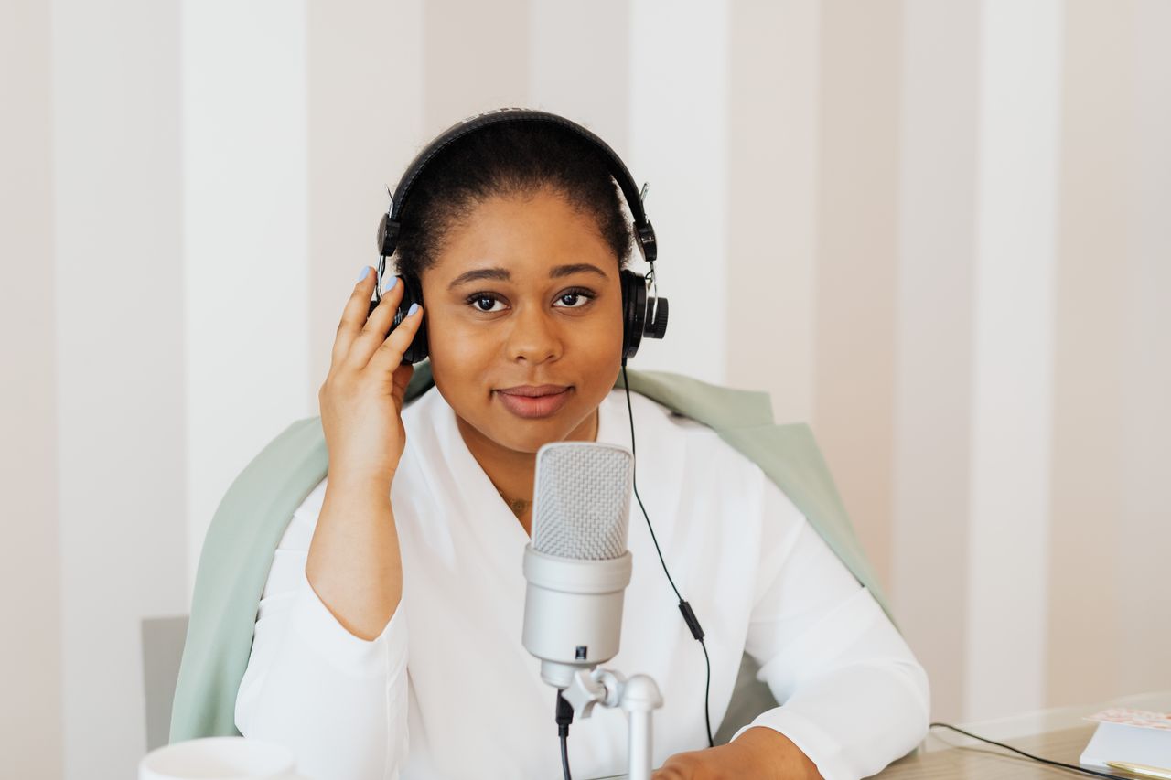 Young woman podcaster with headphones at a desk using a microphone.
